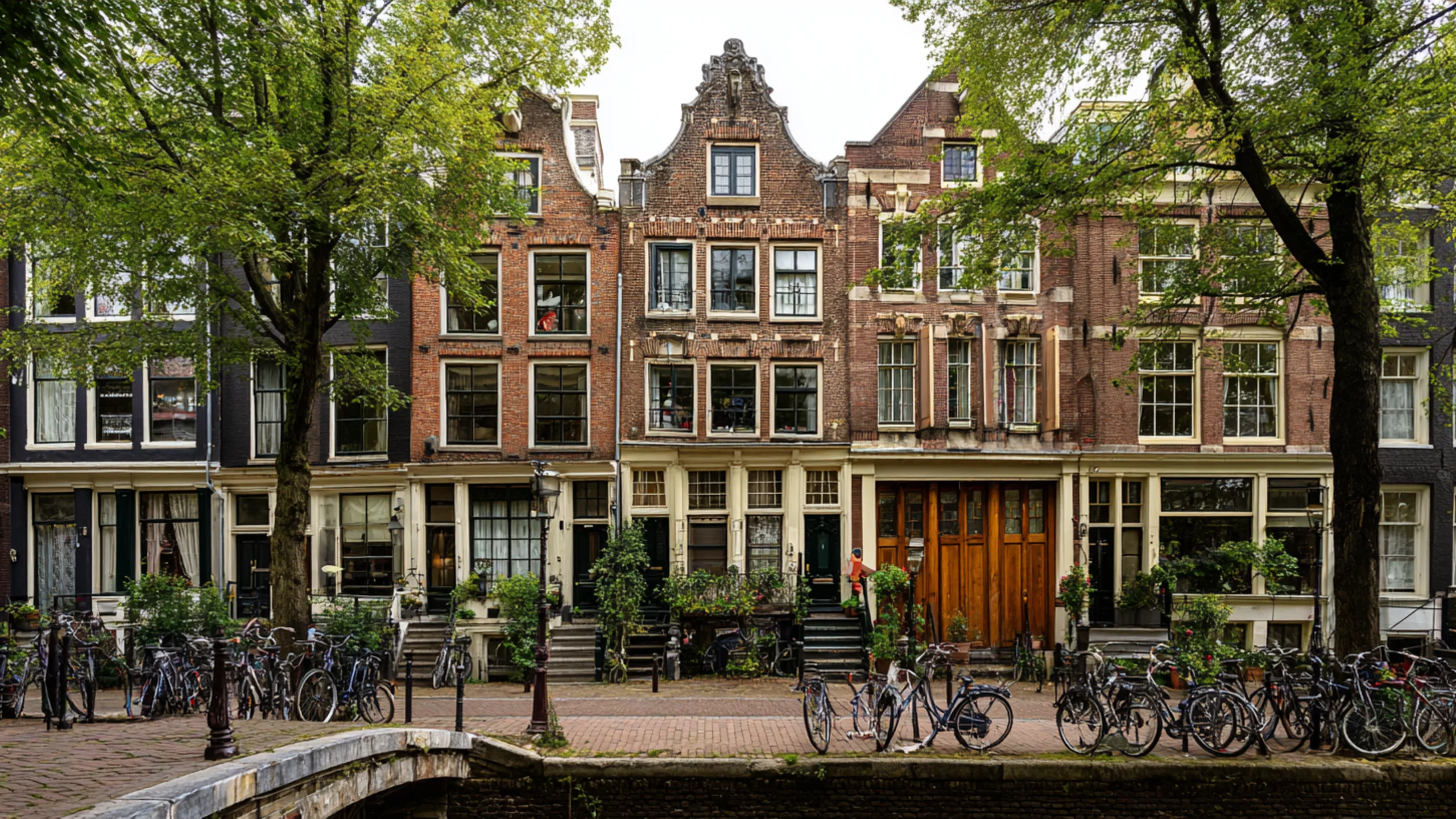 Evening light on an Amsterdam canal with bicycles, brick row houses, trees, and people walking along the water